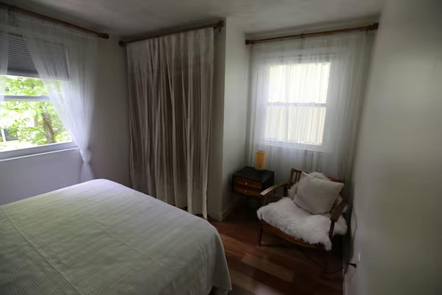 Quarto com cama, cadeira, mesa de cabeceira e janela com cortinas.