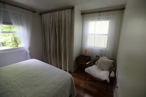 A bedroom with a bed, a chair, a nightstand, and a window with curtains.