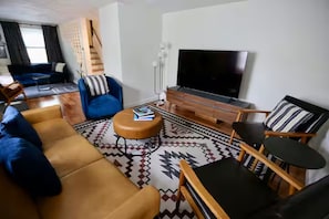 A modern living room with a sofa, ottoman, chairs, a coffee table, and a flat-screen TV.