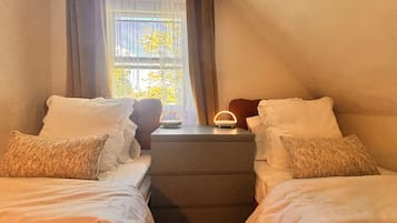 A bedroom with two beds, a nightstand, a lamp, and a window with curtains.