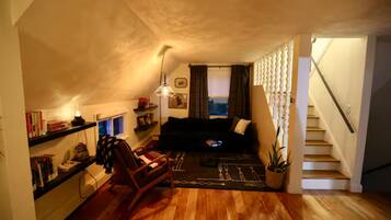 A cozy living room with a wooden floor, a sofa, a rocking chair, and a staircase leading upstairs.