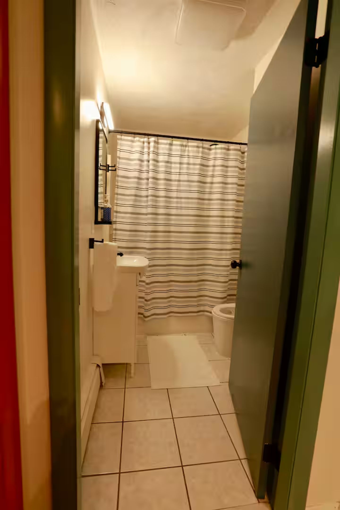 Ein schmales Badezimmer mit Toilette, Waschbecken und Duschvorhang.