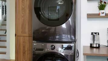 A stacked washer and dryer unit in a modern kitchen with a wooden cabinet and a small countertop with a coffee maker.