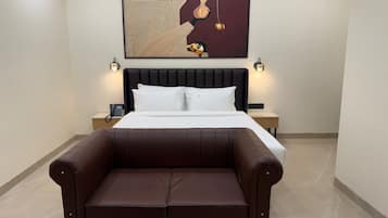 Una habitación de hotel moderna con una cama grande, dos mesitas de noche, una obra de arte en la pared y un sofá de cuero marrón.