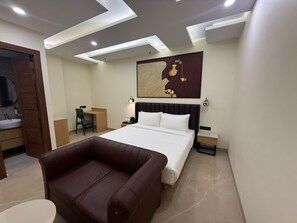 Moderni hotellihuone, jossa on sänky, työpöytä, tuoli, sohva ja suuri, abstrakti taulu seinällä.