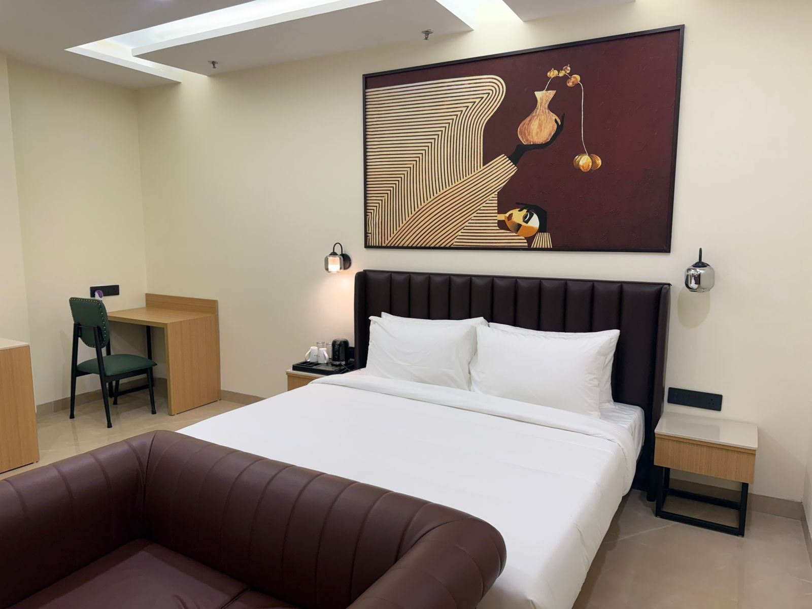 A hotel room with a bed, a desk, a chair, a nightstand, and a large abstract painting on the wall.