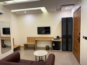Moderni hotellihuone, jossa on sänky, työpöytä, televisio, kahvinkeitin ja pieni jääkaappi.