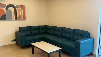 Una sala de estar con un sofá seccional verde oscuro, una mesa de centro de color claro y un cuadro abstracto moderno en la pared.