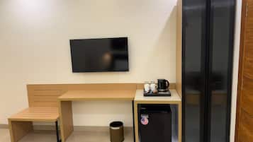 Una habitación pequeña con un banco de madera, un refrigerador negro, una cafetera y un televisor en la pared.