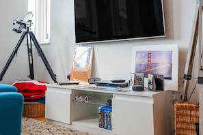 A room with a mounted telescope, a flat-screen TV, a framed picture of the Golden Gate Bridge, a desk with a keyboard, mouse, and books, and a wicker chair. - Bright & Stylish 1-Bed Flat in Central Watford - Pass the Keys (St Albans)