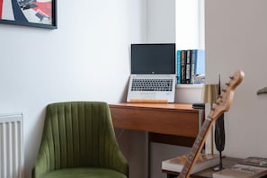 A workspace with a laptop, books, a guitar, and a green chair. - Bright & Stylish 1-Bed Flat in Central Watford - Pass the Keys (St Albans)