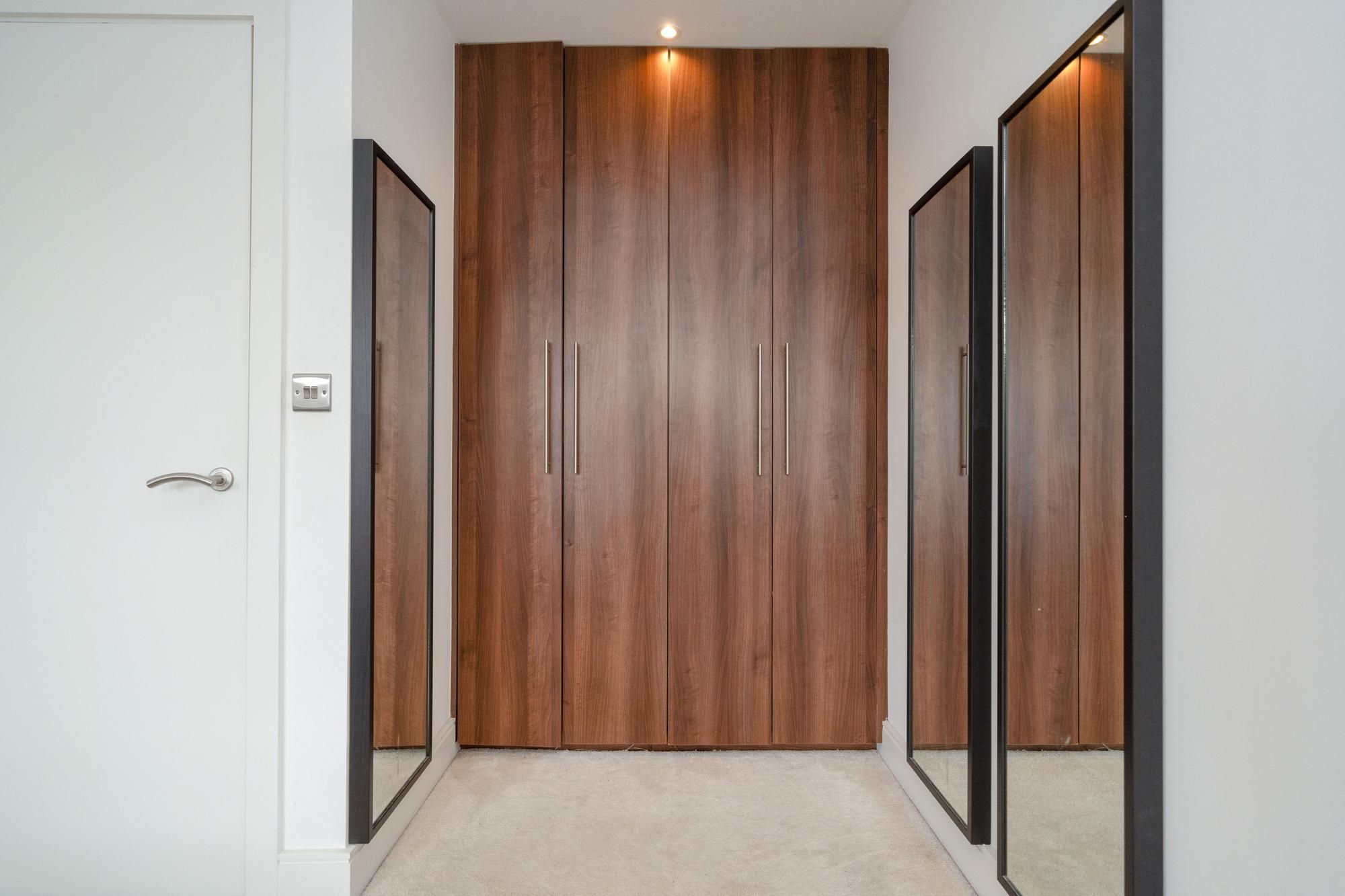 A hallway with a wooden wardrobe, a door, and a mirror.