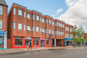 A multi-story building with a brick facade, storefronts on the ground floor, and a clear sky above. - Bright & Stylish 1-Bed Flat in Central Watford - Pass the Keys (St Albans)