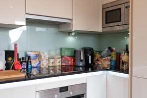 A kitchen with a microwave, coffee maker, and various food items on the counter. - Bright & Stylish 1-Bed Flat in Central Watford - Pass the Keys (St Albans)