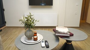 Una sala de estar moderna con un televisor de pantalla plana montado en la pared, una mesa de centro redonda, una mesita auxiliar con un jarrón de plantas verdes, una vela y un control remoto.