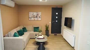 A modern living room with a sofa, a coffee table, a painting, a potted plant, and a door.