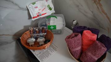 A bathroom with a marble wall, a basket of toiletries, a white bag, a green first aid kit, and a bowl of towels.