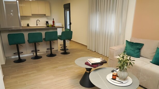 Un espacio moderno para el día a día con un sofá, una mesita de centro con libros, un florero con planta y una cocina al fondo.