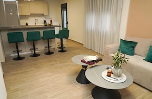 Un espacio moderno para el día a día con un sofá, una mesita de centro con libros, un florero con planta y una cocina al fondo.