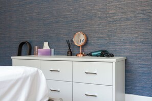 A white dresser with drawers, a mirror, a tissue box, a black hairbrush, a teal hairdryer, and a black candle holder with a candle. - Modern Cosy Home w/ Stylish Interior - Pass the Keys (Borehamwood)