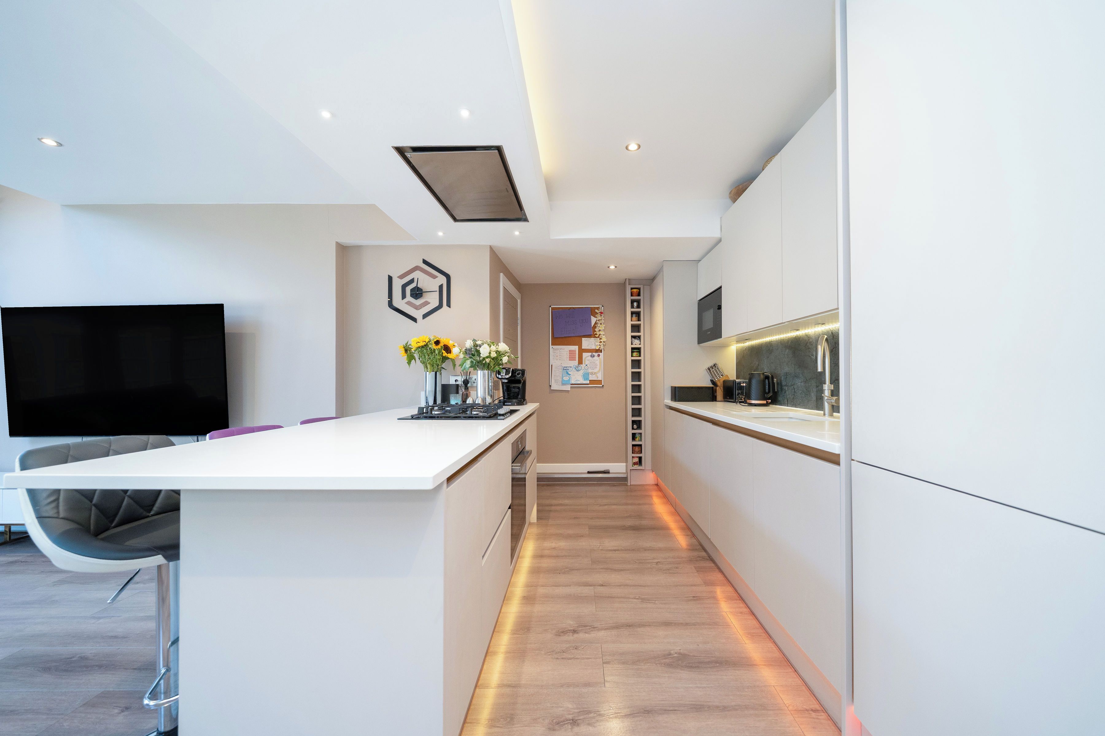 A modern kitchen with a central island, built-in appliances, and a flat-screen TV mounted on the wall.