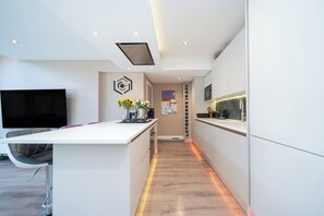 A modern kitchen with a central island, built-in appliances, and a flat-screen TV mounted on the wall. - Modern Cosy Home w/ Stylish Interior - Pass the Keys (Borehamwood)