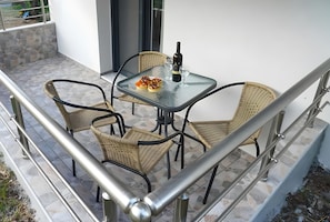 Un balcón con una mesa de vidrio, sillas de mimbre y una botella de vino.