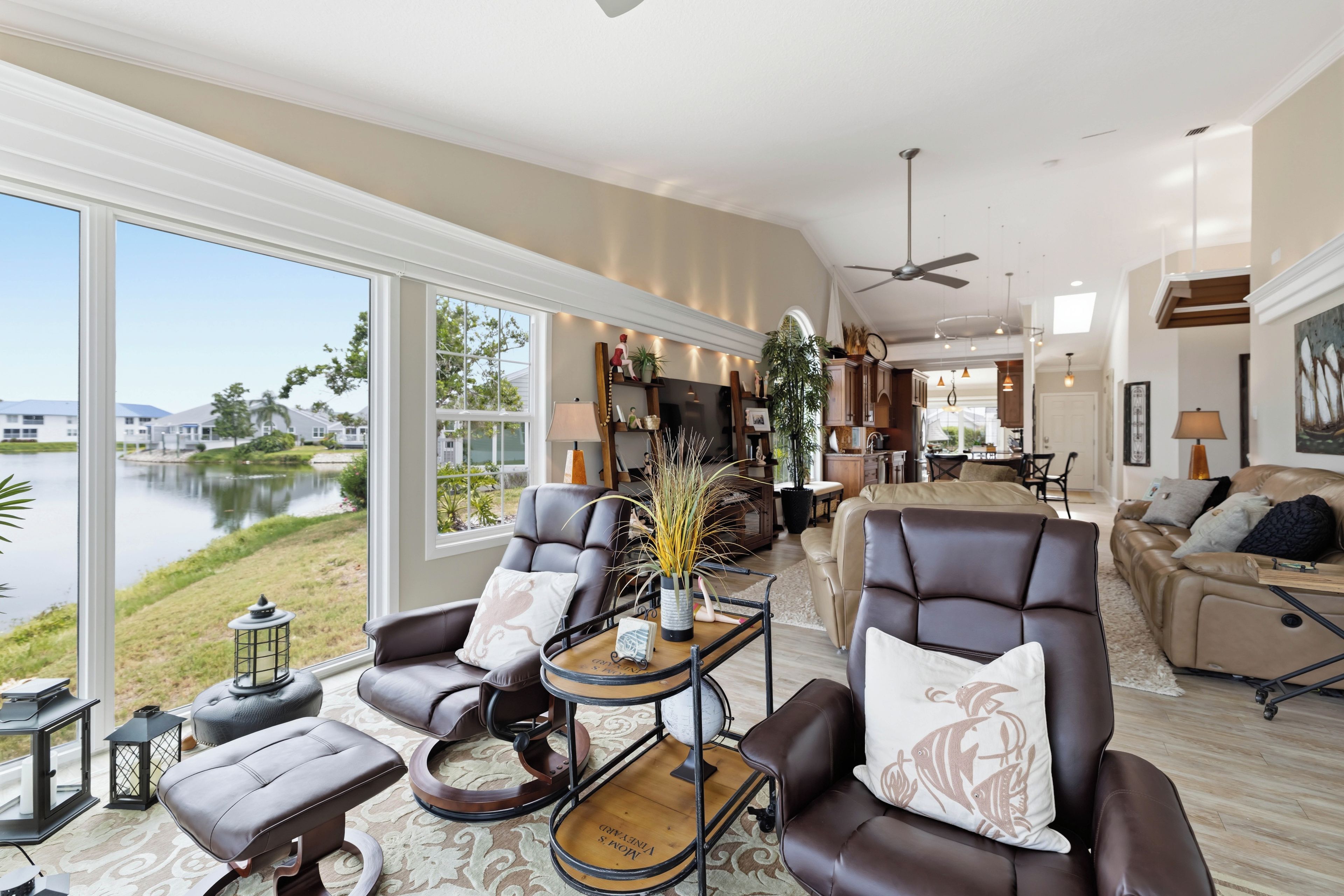 A spacious living room with a view of a lake, leather furniture, and a dining area in the background.