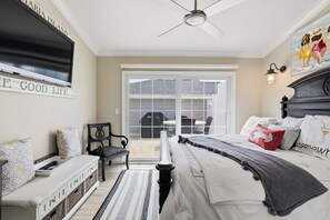 Ein Schlafzimmer mit einem Bett, einem an der Wand befestigten Fernseher, einem Deckenventilator und Blick ins Freie durch eine Schiebetür.
