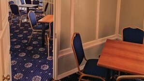 Een hotelkamer met een eethoek, een houten tafel en blauwe fauteuils.