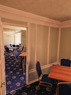 Quarto de hotel com área de refeições, mesa de madeira e cadeiras estofadas em azul.