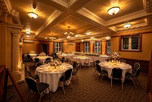 A banquet hall with multiple round tables set for dining, featuring floral centerpieces and candles.