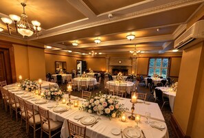 Ein Festsaal mit runden Tischen, Kronleuchtern und floralen Tischdekorationen.