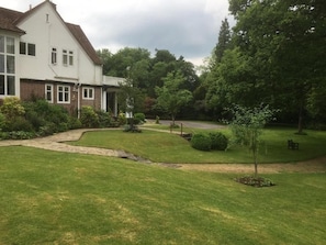 A residential property with a well-maintained lawn, a pathway leading to a house, and a variety of trees and shrubs.