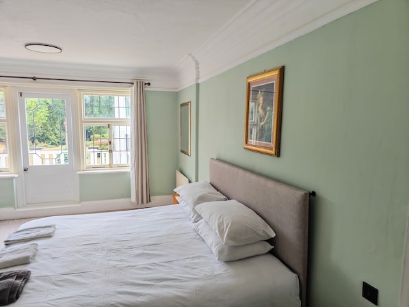 A bedroom with a bed, a window with curtains, a radiator, and a framed picture on the wall.