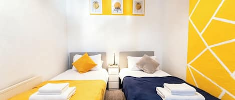 Une chambre d’hôtel avec deux lits, chacun agrémenté d’une serviette soigneusement pliée, une table de chevet avec une lampe et un mur orné de trois tableaux encadrés.