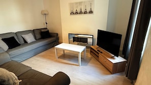 Una sala de estar con un sofá, una mesa de centro, un televisor sobre un mueble de madera y una chimenea.
