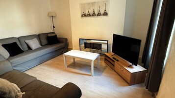 Una sala de estar con un sofá, una mesa de centro, un televisor sobre un mueble de madera y una chimenea.