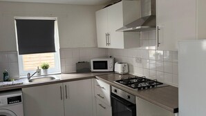 A compact kitchen with white cabinets, a microwave, a toaster, and a gas stove. - House Sleeps 7 With Parking (Wallasey)