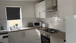 Una cocina compacta con muebles blancos, microondas, tostadora y cocina a gas.
