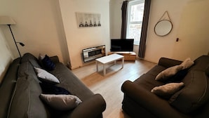 A living room with two sofas, a coffee table, a TV, and a fireplace. - House Sleeps 7 With Parking (Wallasey)