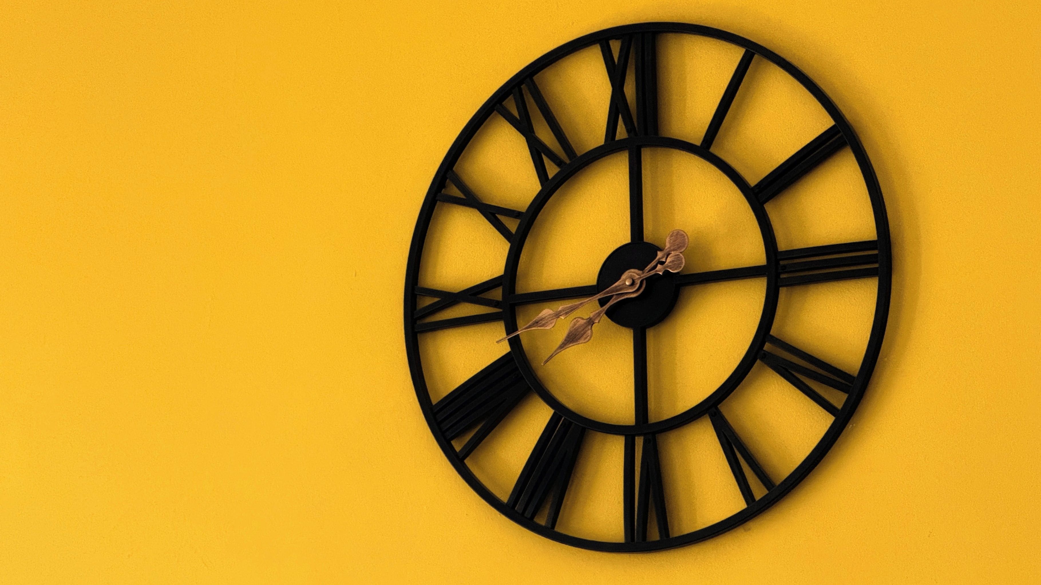 A wall-mounted clock with Roman numerals and a leaf-shaped hand decoration.