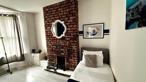 Un dormitorio moderno con chimenea de ladrillo, una cama con ropa blanca y un cuadro en la pared.