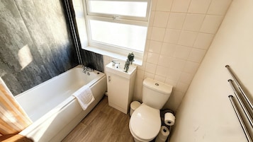 A bathroom with a bathtub, toilet, sink, and window.