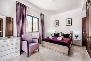 Habitació d'hotel amb un llit, una cadira, un taulell i dues imatges emmarcades a la paret.