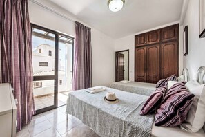 A bedroom with a bed, a wardrobe, a table with a hat, and a view of buildings outside. - Villa Lanzarote - Four Bedroom Villa, Sleeps 8 (Albufeira)
