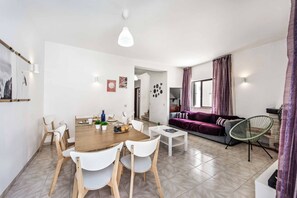 A modern living space with a dining area, a sofa, and a kitchen visible through an open doorway. - Villa Lanzarote - Four Bedroom Villa, Sleeps 8 (Albufeira)