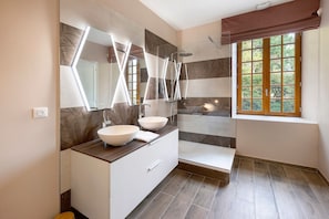 Ein modernes Badezimmer mit zwei Waschbecken, einer Dusche und einem Fenster mit Blick auf Grünflächen.