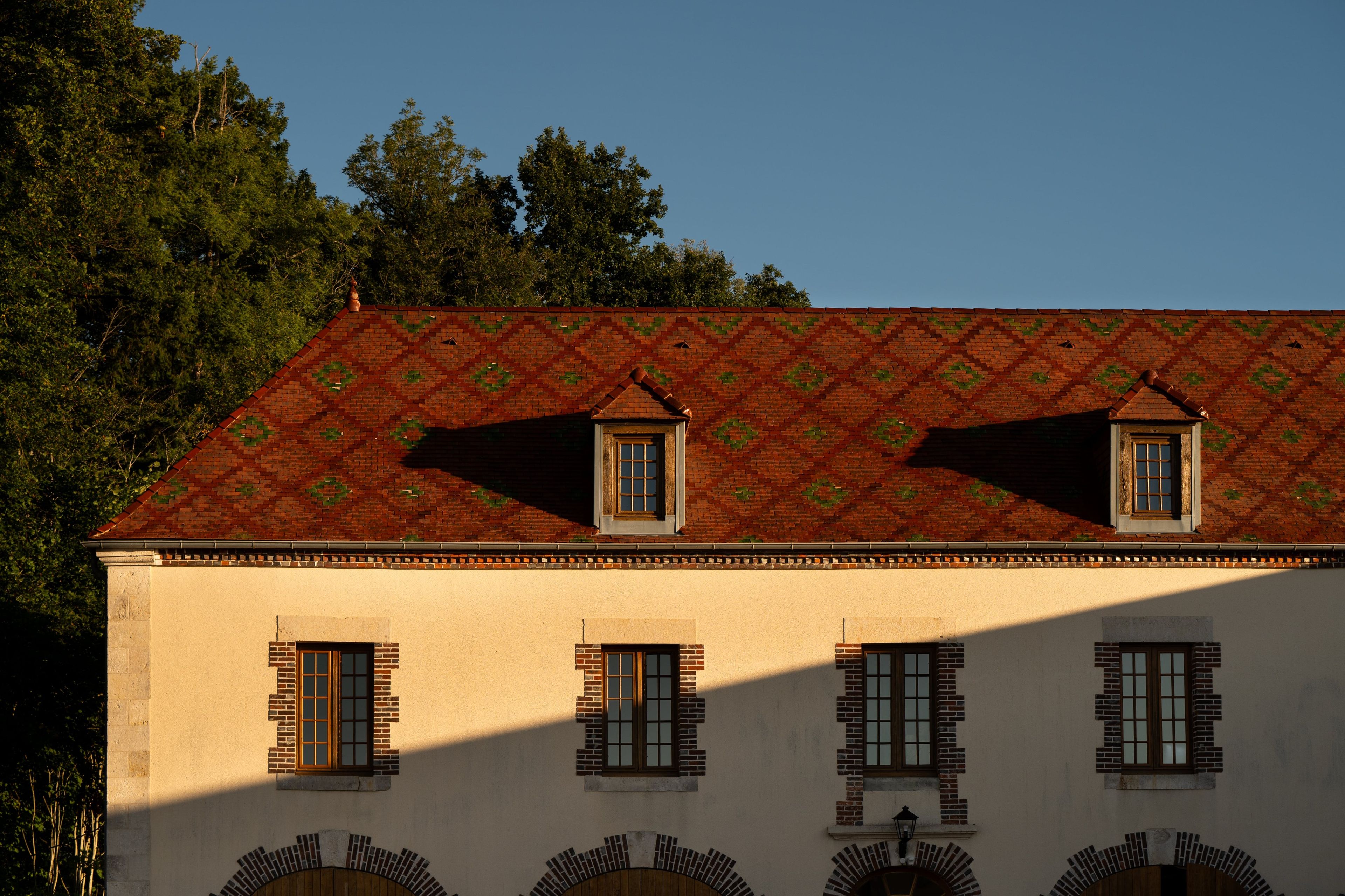 Ein Gebäude mit einer symmetrischen Fassade, zahlreichen Fenstern und einem gemusterten Dach.