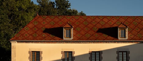 Ein Gebäude mit einer symmetrischen Fassade, zahlreichen Fenstern und einem gemusterten Dach.